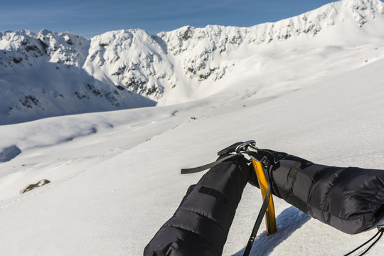 Down mittens clipped carabiner on a yellow ice axe and a ridge in the background.