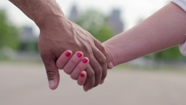 Close up on hands of a mixed race couple.  Slow motion with shallow focus.  Detroit city skyline in soft focus in background.  Recorded hand-held at 60fps in 4K.