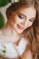 Portrait of pretty young girl in a white dress and long blonde hair surrounded by flowers