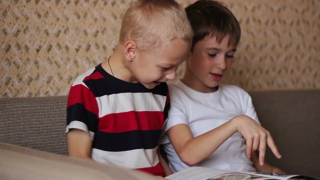 Two boys sitting on a couch and read a book smiling