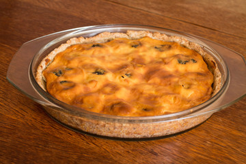 Cake with cottage cheese and prunes in glass brazier on wood table.