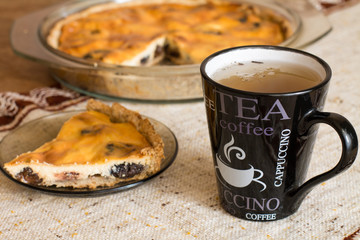 Part of cake with cottage cheese and prunes in plate and cup of tea