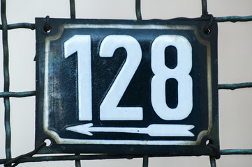 Weathered grunge square metal enameled plate of number of street address with number 128 closeup