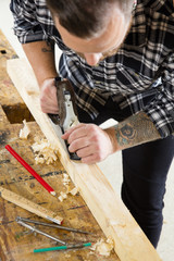 Focused craftsman working with plane on wood plank in workshop