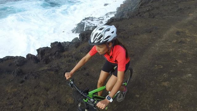 Mountain biking woman cycling on MTB Bike trail steep cliff path on mountain by the sea. High angle view of cyclist riding bicycle in nature. Female biker living healthy lifestyle. ACTION CAMERA.