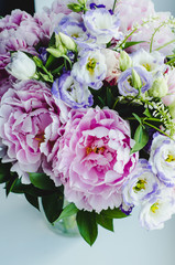 Rich bunch of pink peonies peony and lilac eustoma roses flowers in glass vase on white background. Rustic style, still life.