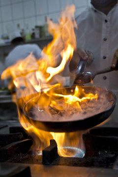Chef in restaurant kitchen at stove with pan, doing flambe on food
