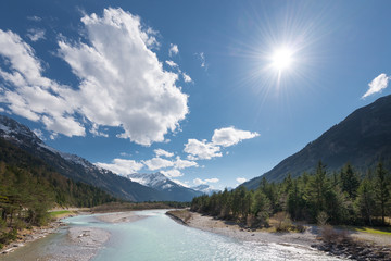 sun and clouds over flowing river at austrian mountains
