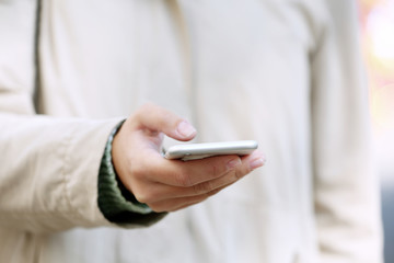 A female hand holding a mobile phone outdoors, on blurred background