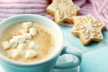Cup of hot cacao with marshmallow, cookies and warm scarf on blue table