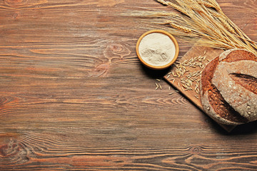 Fresh baked bread, a bowl of flour and wheat ears on the wooden background