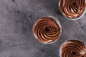 Three chocolate cupcakes on grey background, close up