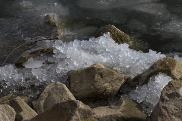 Naklejka premium Ice crushed on the rocks along the shoreline of a partially frozen lake.