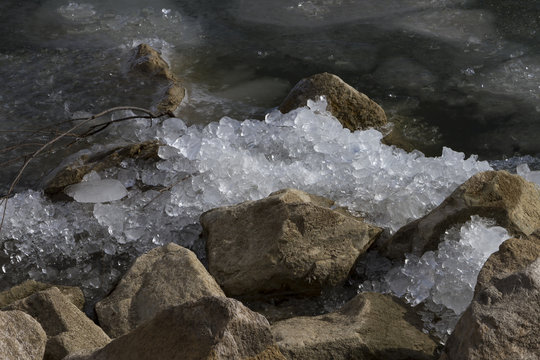 Ice crushed on the rocks along the shoreline of a partially frozen lake.