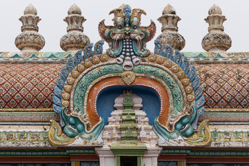 Fototapeta na wymiar Trichy, India - October 15, 2013: Closeup of bow decoration on the Vimanam of one Gopuram at Shirangam temple. Monster face on top of bow with bulk of brown-beige vimanam as background.