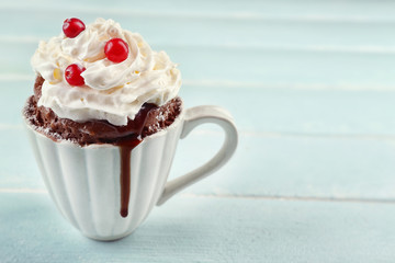Mug cake with cream and cranberry on blue wooden background
