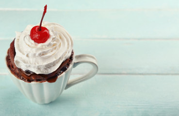 Chocolate mug cake with cream and cherry on blue wooden background