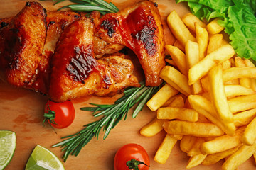 Grilled chicken wings with French fries and garden-stuff on cutting board