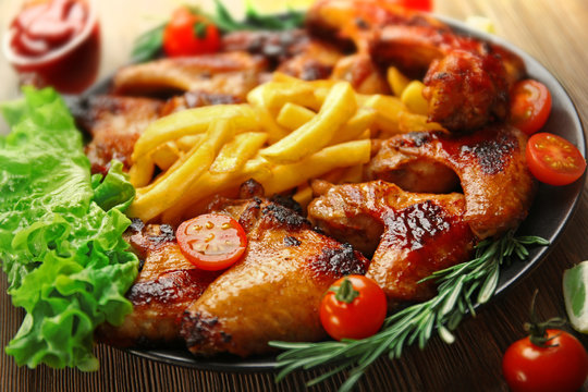 Grilled chicken wings with French fries, garden-staff and tomatoes on plate