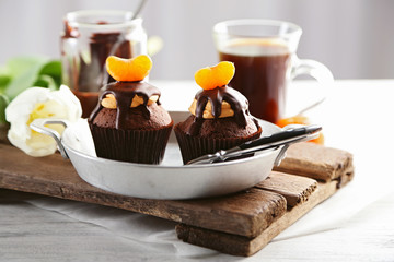 Two tasty cupcakes with slice of mandarin and chocolate on a pan, close up