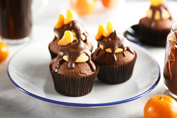 Three tasty cupcakes with slice of mandarin and chocolate on a plate, close up