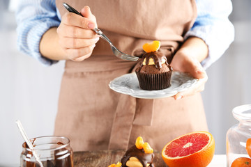 Female baker decorating tasty cupcake with slice of mandarin and chocolate on the table