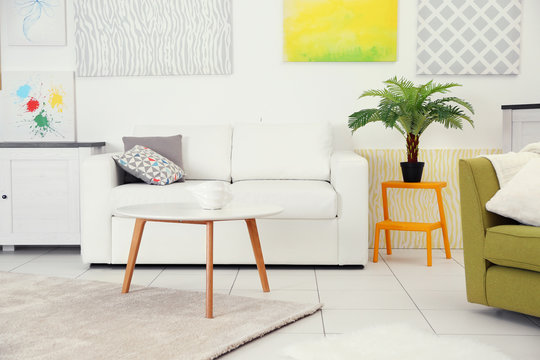 Modern living room interior with white sofa, coffee table and canvases on the white wall