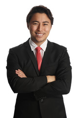 Smiling businessman looking at camera, wearing a black suit, white shirt and a red tie. Standing in front of a white background.