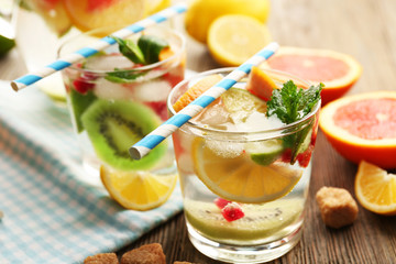 Refreshing cocktails with ice, mint, pomegranate seeds and slices of fruits on wooden background