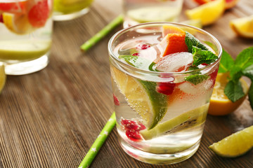 Refreshing cocktail with ice, mint, pomegranate seeds and slices of fruits on wooden background