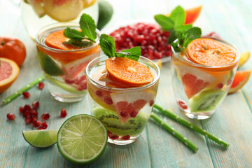 Refreshing cocktails with ice, mint, pomegranate seeds and slices of fruits on blue wooden background