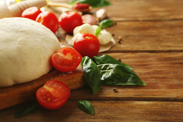 Pizza dough with tomatoes, green basil and Mozzarella on wooden background