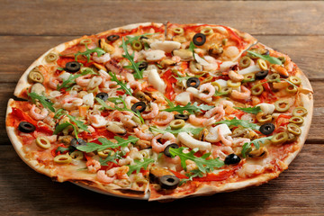 Pizza with seafood, red pepper and olives on wooden table