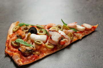 Pizza slice with seafood, red pepper and olives on grey background