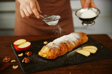 Woman powdering an apple roll with a sugar powder