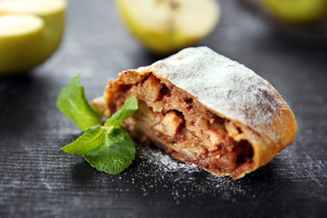 Slice of strudel with apples, walnut and raisins on dark wooden table