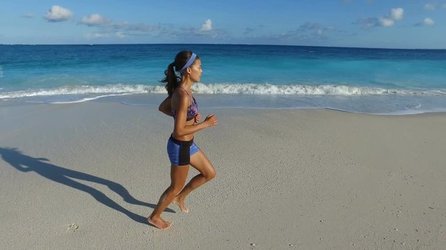 Jogger running on idyllic beach. Young woman runner jogging determined on sea shore. Fit female in sportswear on idyllic beach exercising in nature during summer. ACTION CAMERA.