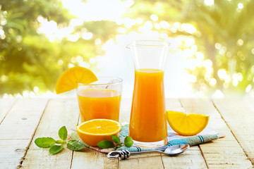 Glass and pitcher of orange juice on wooden, on green nature background