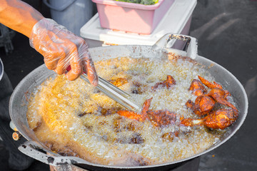 Hand with glove frying chicken in a wok