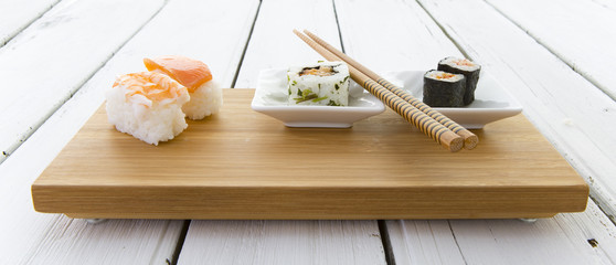 Sushi served on a Bamboo board with chopsticks on a rustic white