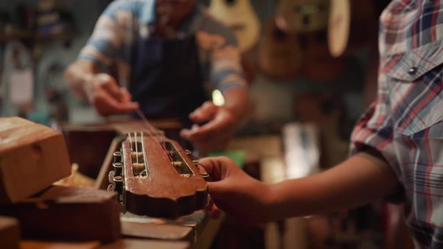 Old and young people showing love for music. Boy and senior man, happy kid and elderly person, grandfather showing guitars and instruments to grandson in lute maker shop. Proud retired worker