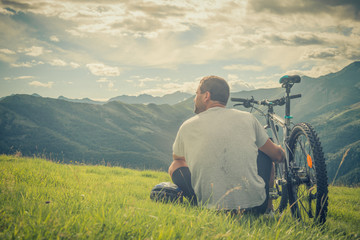 Fototapeta na wymiar Young man sitting near bike looking at panorama on mountain