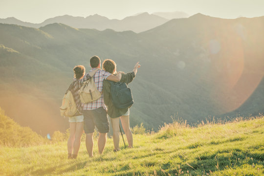 Three friends stand looking at panorama on mountain