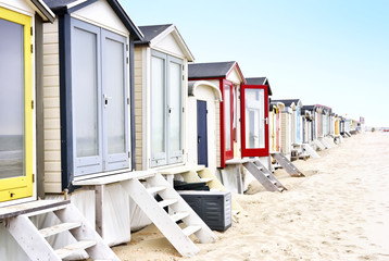Fototapeta na wymiar Beach huts or houses and blue sky. Multicolored beach bathing huts with white sand and clear blue sky. Beach scene with copy space. Side view of beach huts in a row.