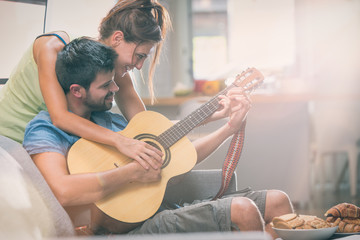 Young couple playing guitar on couch indoor