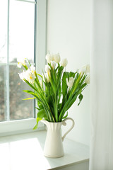 white tulips, and irises are in a vase on the window