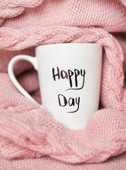 cup with the inscription happy day wrapped in a warm pink sweate