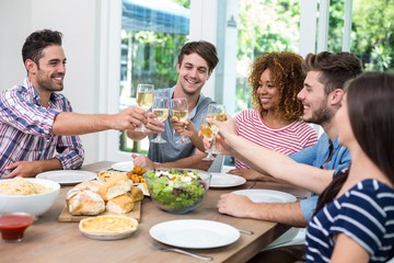 Young friends toasting wine while having meal at table