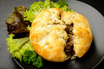 Pie with minced meat on black plate.