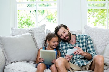 Father showing mobile phone to daughter while sitting on sofa